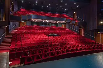 Zaalaanzicht van de rode stoelen, gezien vanaf de zijkant van het podium.
