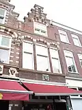 Pand met trapgevel. Dubbele midden pinakel op twee leeuwenconsoles rustend. Bogen boven de ramen met leeuwemaskers, versieringen, natuursteen blokken