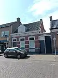 De voorgevel heeft gepleisterde speklagen en een kordonlijst, die ter hoogte van de vensteropeningen overgaat in een hardstenen lekdorpel.