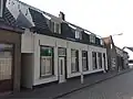 Twee woonhuizen gebouwd circa 1900 met mogelijk een oudere kern onder een mansarde kap die evenwijdig loopt aan de straat.