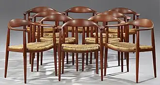 Foto van tien stoelen die gemaakt zijn van donker hout en een rieten zitting hebben. De rugleuningen zijn rond en lopen over in de armleuningen. De foto van de stoelen is genomen tegen een grijze achtergrond.