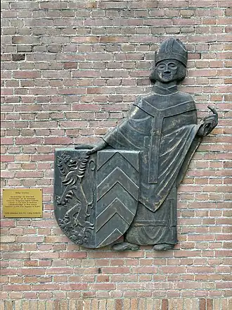 Reliëf van het wapen van de voormalige gemeente Hoogeloon, Hapert en Casteren met Sint Severinus geplaatst bij het kerkgebouw.