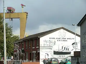 Een muurschildering in Belfast van Harland en Wolff met op de achtergrond een stukje van een portaalkraan