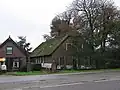 Boerderij onder rieten wolfdak. Links onderkelderd; vensters met zes- en vierruitsschuiframen. Links zomerhuis onder zadeldak. Twee moderne hekpijlers, waarop gebeeldhouwde leeuwen met wapenschilden