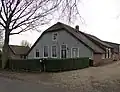 Boerderij, onder rieten wolfdak en met gepleisterde voorgevel. In de rechter zijgevel onder een opgewipt dak twee vensters met luiken en 20-ruitsroedenverdeling in de schuiframen
