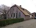 Boerderij, onder rieten wolfdak. In de gepleisterde voorgevel vensters met luiken en een zoldervenster met half kruiskozijn en onderluiken. Links een opkamer
