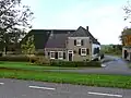 Boerderij bestaande uit grote gemetselde stal-schuur onder rieten wolfdak, en uit een woonhuiscomplex waarvan het hoofdgedeelte een voor- en achtergevel met ingezwenkte bovenhoeken en met kroonlijst heeft