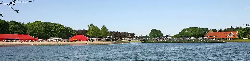 Panorama van recreatiegebied met op de voorgrond water en links feesttenten