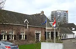 Boerderij, bestaande uit woonhuis met driezijdig uitgebouwde voorkamer, schilddak en vensters met blinden en negenruitsschuiframen, alsmede uit een langgerekte stal onder pannen zadeldak. Bij het woonhuis een deur met panelen in omlijsting van pilasters met hoofdgestel. Zesruitsbovenlicht