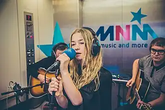 Luka Cruysberghs (toenmalig zangeres) met Hooverphonic in 2018 tijdens een 'liftconcert' bij MNM.