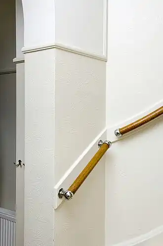 Een witte wenteltrap met houtkleurige leuning, een witgeverfde houten smetplank tegen een muur met een delicaat wit patroon.