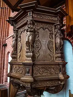 Kuip met kariatiden: Links en midden respectievelijk de christelijke deugden 'Hoop' en 'Liefde' en rechts de kardinale deugd 'Rechtvaardigheid' Onder deze kariatiden is een bladmasker, ook bekend als groene man, aangebracht.