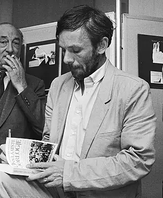 John Jansen van Galen signeert zijn boek 'Ons laatste oorlogje' (1984), achter hem, een sigaret rokend, Edzo Toxopeus