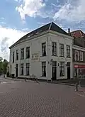 Hoekpand met gepleisterde lijstgevels met smalle gevel aan de Veenestraat en zijgevel aan de Burgwal onder langgerekt schilddak
