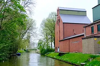 Voormalige veevoederfabriek van Jacobus Jan Nienoord aan het kanaal in Baflo met op de achtergrond het hoogholtje tussen Baflo en Rasquert
