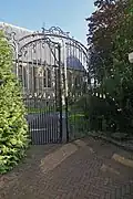 Nederlands Hervormde Kerk: smeedijzeren toegangshek, uitgevoerd in Lodewijk XV-stijl, met gebogen zijstukken en top, versierd met voluten en rocaillemotieven, deels verguld