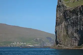 Een klif van Svínoy met op de achtergrond het dorp Kirkja op Fugloy