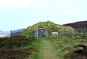 De Knowe of Yarso Chambered Cairn ligt op een klifrand en wordt beschermd door een moderne betonnen constructie.