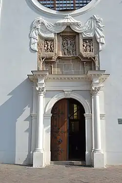 Het portaal boven de hoofdingang, onder een barok baldakijn, verbeeldt de kruisiging op de Calvarieberg.