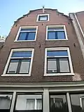 Pand, later met een verdieping verhoogd huis, waarvan de gevel wordt afgesloten door een uit- en ingezwenkte top onderrollagen