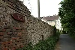 Muur van voormalige suikerfabriek met plaatsnaambordje - op achtergrond Vila Varvažov