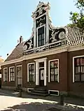 Bakstenen huis, waarvan de brede voorgevel een middenrisaliet heeft, bekroond met een zeer rijk versierd voorschot met Lodewijk XV- en Lodewijk XVI-motieven