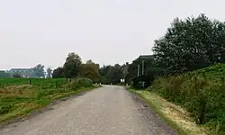 Dijkcoupure met schotbalkhuisje (nu bankje) en links op de achtergrond gemaal De Waterwolf