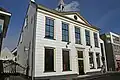 Voormalig gemeentehuis. Witgepleisterde gevel met driehoekig fronton, gesneden deur en kalf en Empire-schuiframen