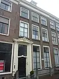 Pand met bakstenen gevel met pilasters en rechte kroonlijst. Hardstenen stoep met palen