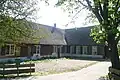 Boerderij. Grote hoeve met puntgevel, waarin ontlastingsbogen. Links een uitgebouwde opkamer. Stal met oude kozijnen en luiken