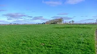 Het terrein van de in de 20e eeuw gesloopte boerderij met boerderij De Juist op de achtergrond. De verhoging achterin het grasland verwijst naar de locatie van de noordwestelijke gracht van de borg De Juist.
