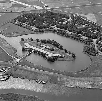 Het Fort benoorden Spaarndam vanuit de lucht gezien; 1977. De foto is naar het westen gericht. Voor het fort het munitieopslagterrein. Verder naar boven de Slaperdijkweg en achter de weg nog enkele groepsschuilplaatsen voor het Fort bezuiden Spaarndam.