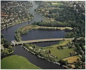 Luchtfoto van De Eenhoorn met op de voorgrond de Schouwbroekerbrug richting Heemstede over de Schouwbroekerplas, een voormalige zandafgraving en vuilstort. Op de achtergrond is molen De Eenhoorn en de bebouwing van buurtschap Zuid-Schalkwijk en stadsdeel Schalkwijk.