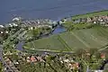 Luchtfoto van een deel van Grünendeich. Links, aan de Elbe, de veerboot aan de steiger, en rechts de stormvloedkering in het riviertje de Lühe.