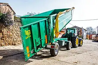Figuur VI: monocoque kipper met twee assen (draaikrans bovenop voorste as) en een hydraulisch openende achterdeur waarop een eendelige wagondeur met graanschuif zit. Let ook op het manueel afdekzeil