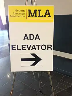 Bord met ADA-tekst en een lift indicatie, bedoeld om aan te geven dat een lift geschikt is voor mensen met een beperking.