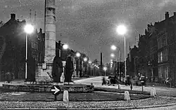 Mariamonument en fabrieks-schoorsteen bij avond, 1956