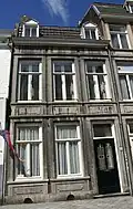 Huis met brede lijstgevel, voorzien van vensters in Naamse steen, in verticale richting met elkaar verbonden door panelen.