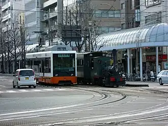 Een tram en het Botchan toeristisch treintje aan de halte Minami-Horibata