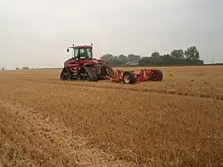 Rode tractor met diepwoeler op een stoppelveld