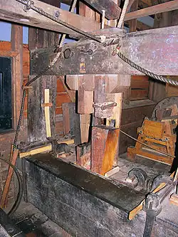 Voorslagblok van De Passiebloem. Boven op de staander staat een houten spanveer, die tegen de blokstut is bevestigd en onder de krul van de jager zit een houten kussendopje. Door het kussendopje glijdt de onderkant van de jager gemakkelijker over de bodem van de laad. Deze voorzieningen zorgen ervoor dat aan het eind van de persing de staander en de jager bij het uithalen van de haar evenwijdig aan elkaar gaan staan, waardoor een haar voor de volgende persing makkelijker tussen de jaagijzers gestoken kan worden.