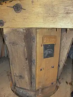 Koker met een stukje van de oude Bremer roede uit 1965 met het roedeplaatje en roedenummer 97 met daarboven het jaartal 2011 met de initialen JNS van de laatste restauratie. JNS zijn de initialen van de zoon van molenaar Aard Schouten.