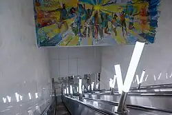 De roltrappen tussen hal en perron onder het mozaïek met dansende wereldburgers.