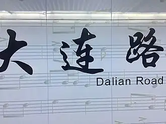 Stationsnaam op de perronwand van de perrons van lijn 12 met de partituur van Mars van de vrijwilligers als achtergrond.