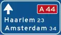 K1: Lage beslissingwegwijzer langs autosnelweg voor de doorgaande richting, met interlokale doelen en routenummer autosnelweg