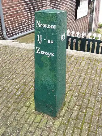 Kilometerpaal van de Noorder IJ- en Zeedijk, naast de brug, voor de sluiswachterswoning