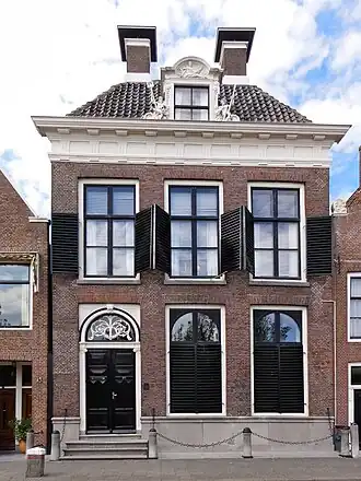 Fors pand met versierde kroonlijst met U-vormig zadeldak onder dwarsdak met twee hoekschoorstenen en dakkapel en groot venster aan achterzijde met uitzicht op zee