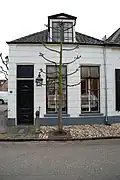 Pand met gepleisterde gevel. Goede vensters en deur. Stoeppaal met kettingen. Keitjesstoep, lindeboom