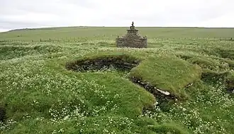 Nybster Broch vanuit het noordoosten. Op de achtergrond staat het monument opgericht ter ere van Sir Francis Tress Barry, die deze vroege broch in 1896 opgroef.