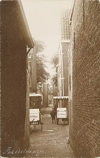 Gezicht in het Fokkestraatje van de Lammermarkt naar de Oude singel. Op de voorgrond 2 karretjes van de firma D.P. Fokkema.